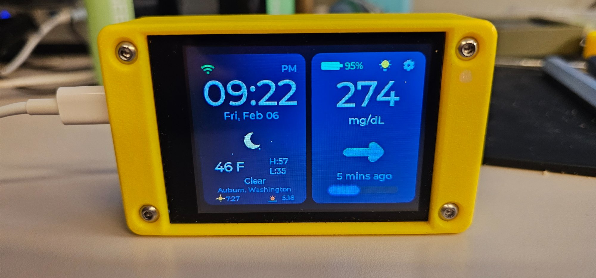 CYGM device showing glucose reading and weather on a yellow 3D-printed case